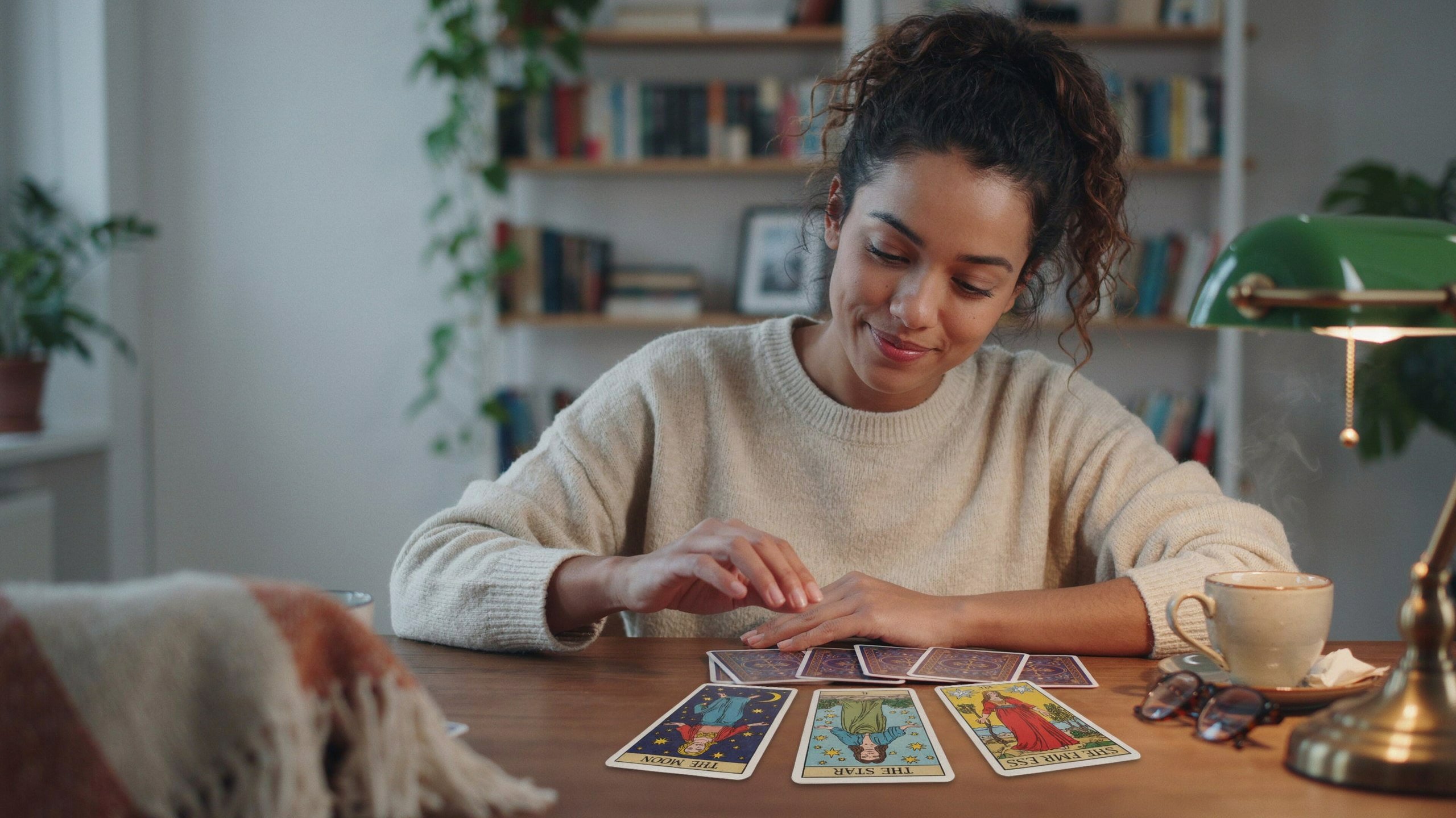 Mulher sorrindo interpretando cartas de tarot sobre mesa de madeira com A Lua e A Estrela invertidas e A Imperatriz